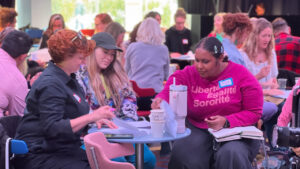 A group of diverse people engaged in conversation at a lively event, with refreshments on tables and vibrant seating around them.