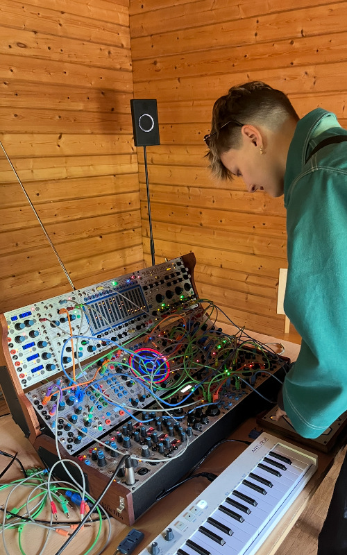 Sonia is standing over a music desk full of colourful wires with a keyboard in next to it