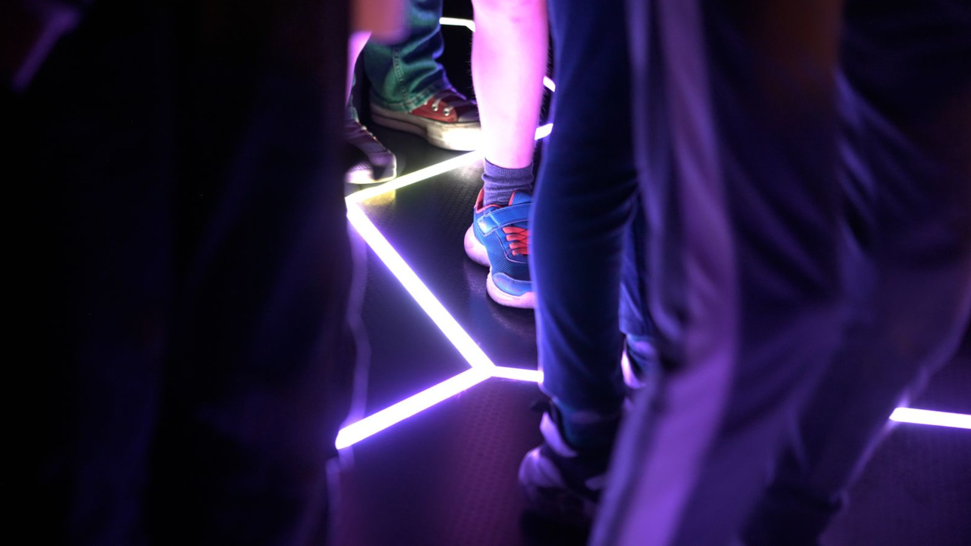 Cropped image of legs and feet on a black floor with a bright purple crack of light glowing from the tiled floor