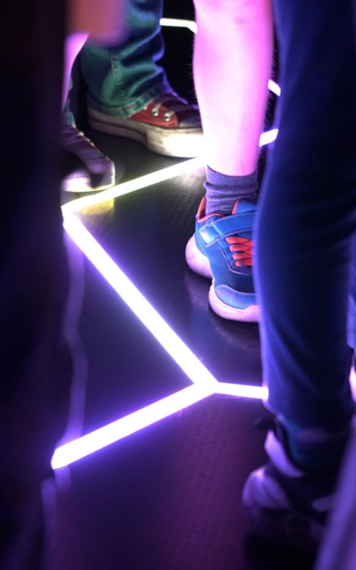 Cropped image of legs and feet on a black floor with a bright purple crack of light glowing from the tiled floor
