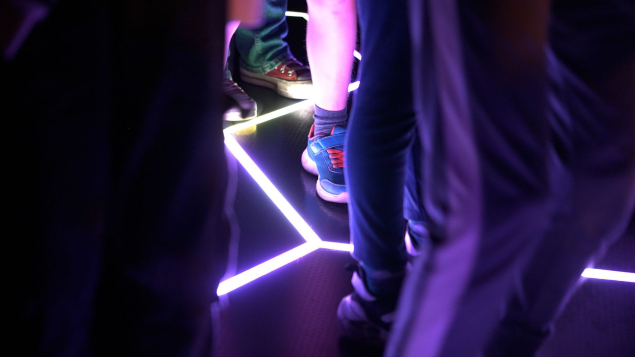 Cropped image of legs and feet on a black floor with a bright purple crack of light glowing from the tiled floor