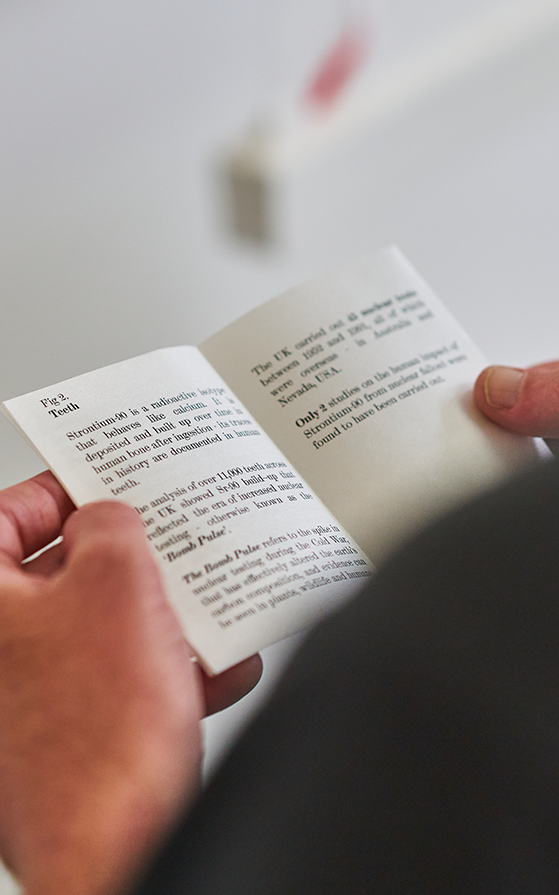 Close-up of hands holding and reading a small open booklet with printed text. The background is softly blurred, creating a focused and introspective mood.