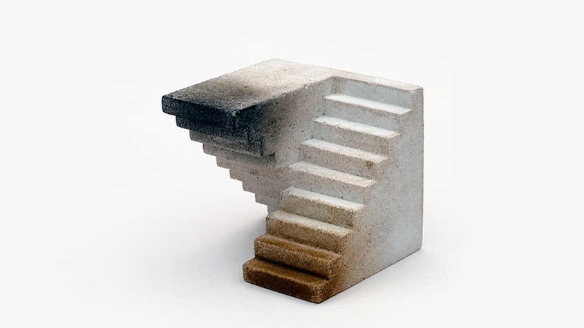 A 3D optical illusion sculpture shows two staircases merging at a right angle. The left is shaded dark, and the right is light, creating a surreal effect.