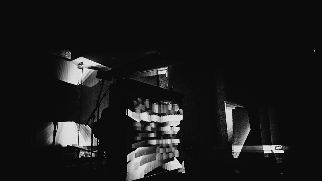 Two people wearing headphones sit inside a bus replica, watching historical footage of buses on screens resembling bus windows. The scene feels immersive.