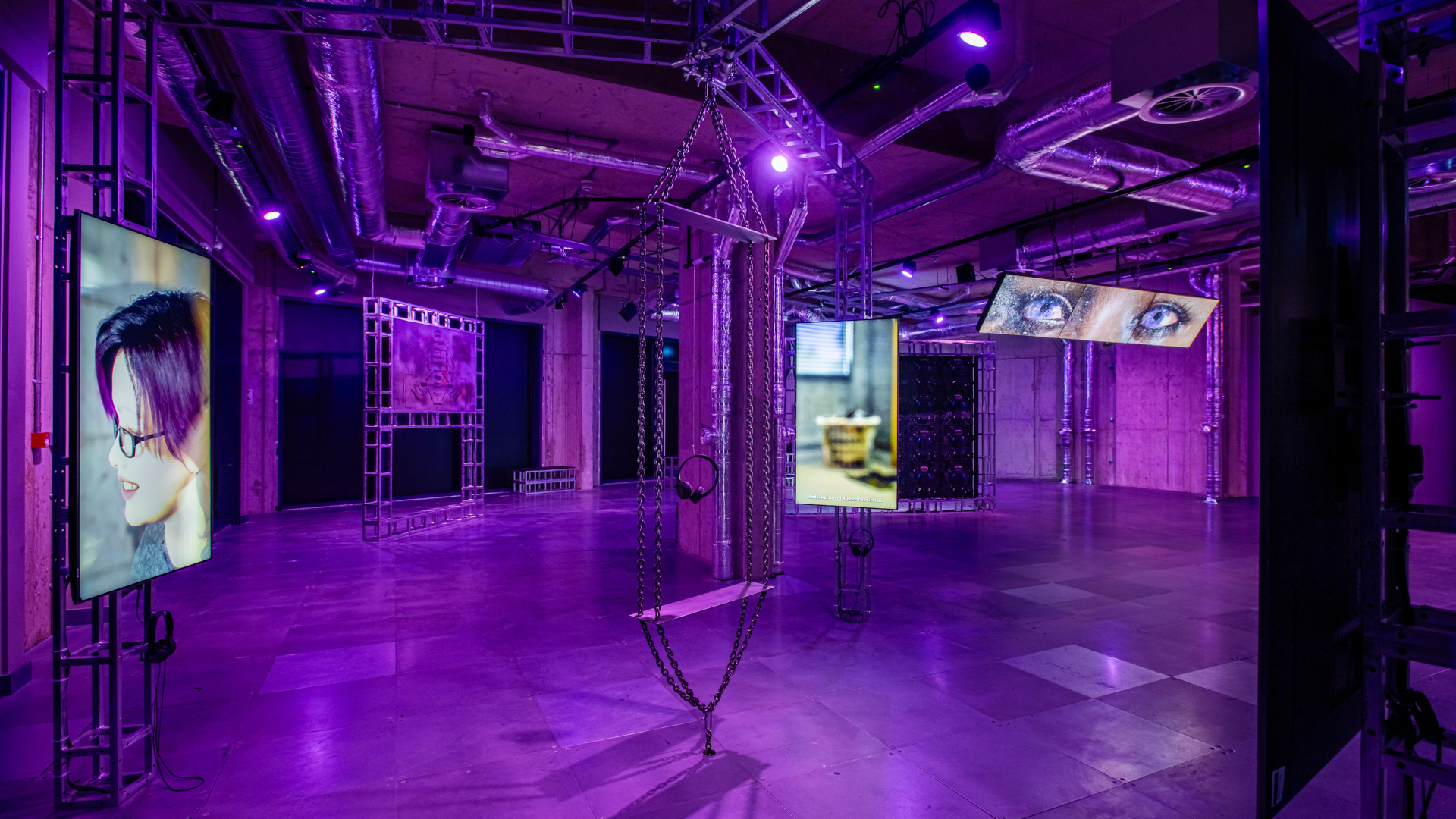 exhibition installation with monitors across a large industrial room lit in purple light
