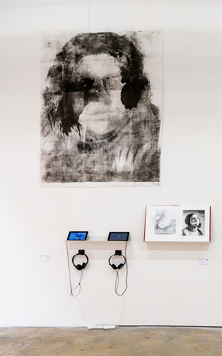 Black and white art exhibit displays abstract portraits of faces with blurred details. Below, two tablets and headphones rest on a minimalist shelf.