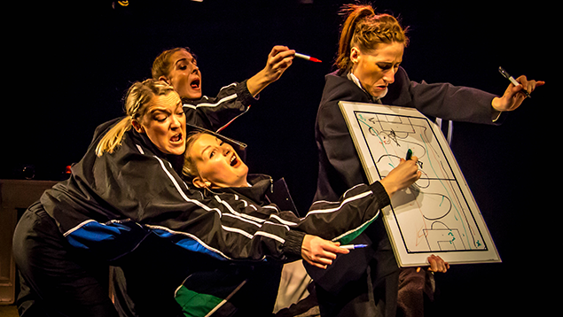 Four people in athletic wear humorously struggle to draw on a whiteboard with sports tactics. The scene is lively, chaotic, and amusing.