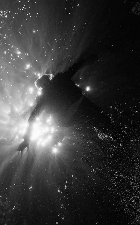 A person in silhouette floats underwater with rays of light streaming down from the surface, creating a serene and ethereal atmosphere.