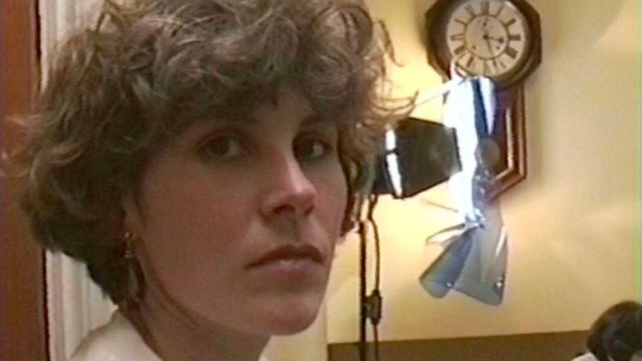 A young white woman looks softly into the camera, she has big brown eyes and short wavy hair.